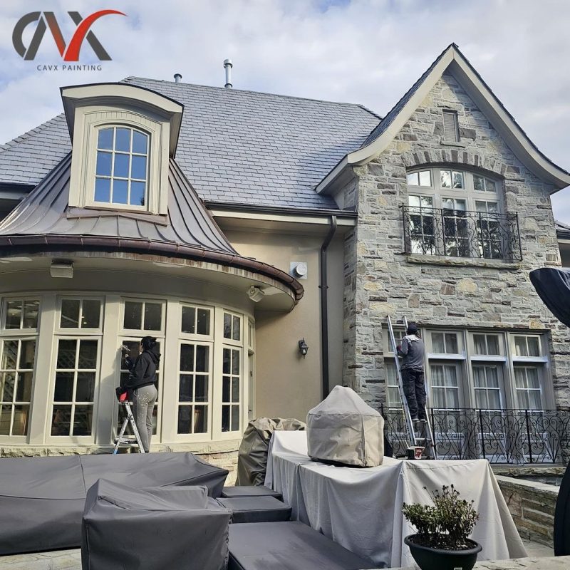 Painters working on exterior detailing of a large stone and stucco house.