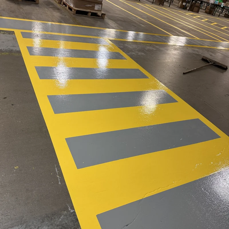 Shiny warehouse floor with yellow and gray safety walkway markings.