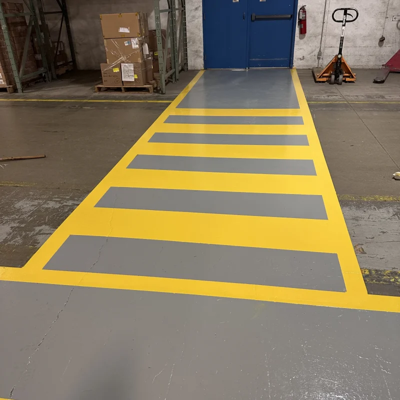Freshly painted industrial walkway with yellow safety borders and gray interior stripes.