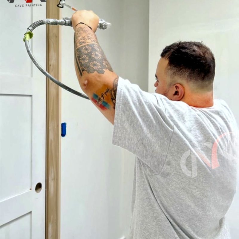 Painter using a spray gun to apply paint on an interior door frame.