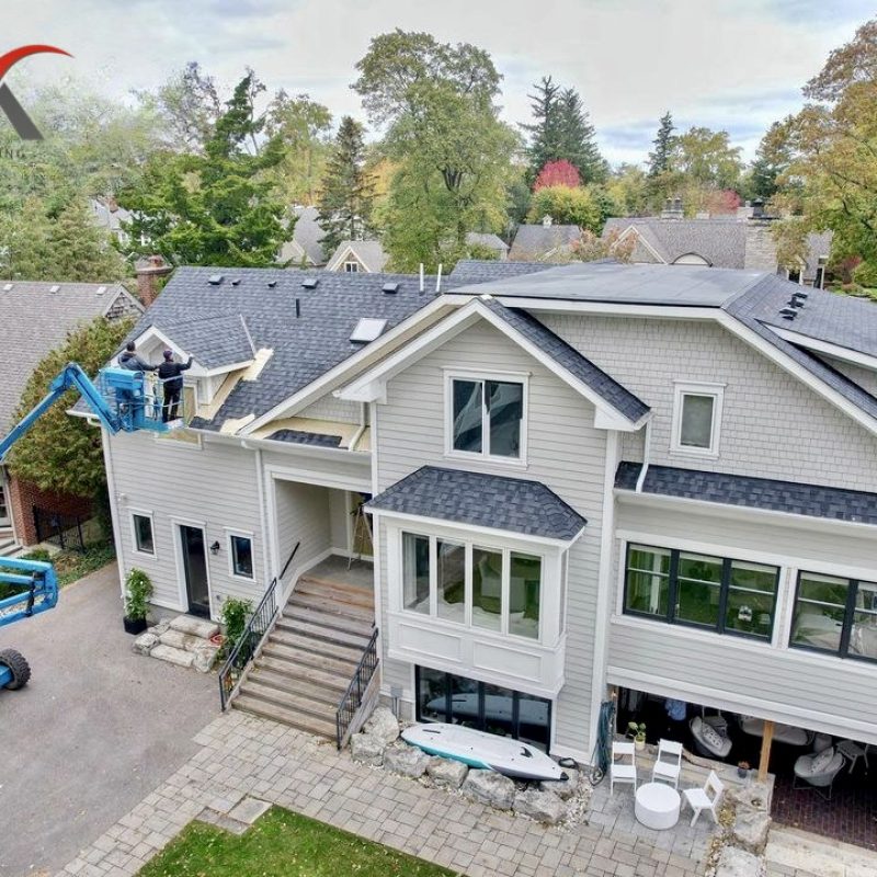 Painters using a lift to work on exterior siding of a large residential home.