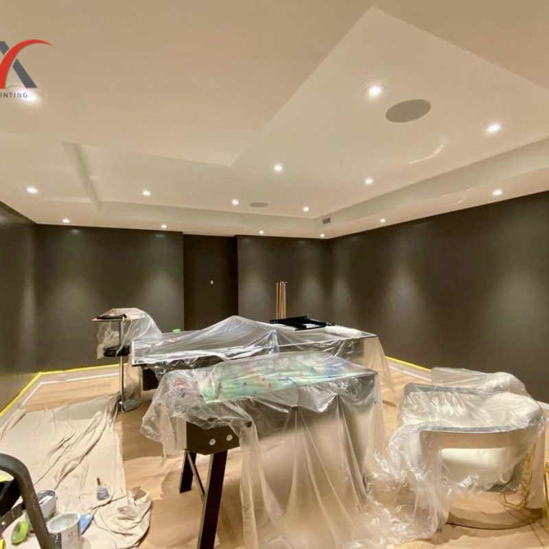 Basement room prepared for painting with furniture covered in plastic sheets.