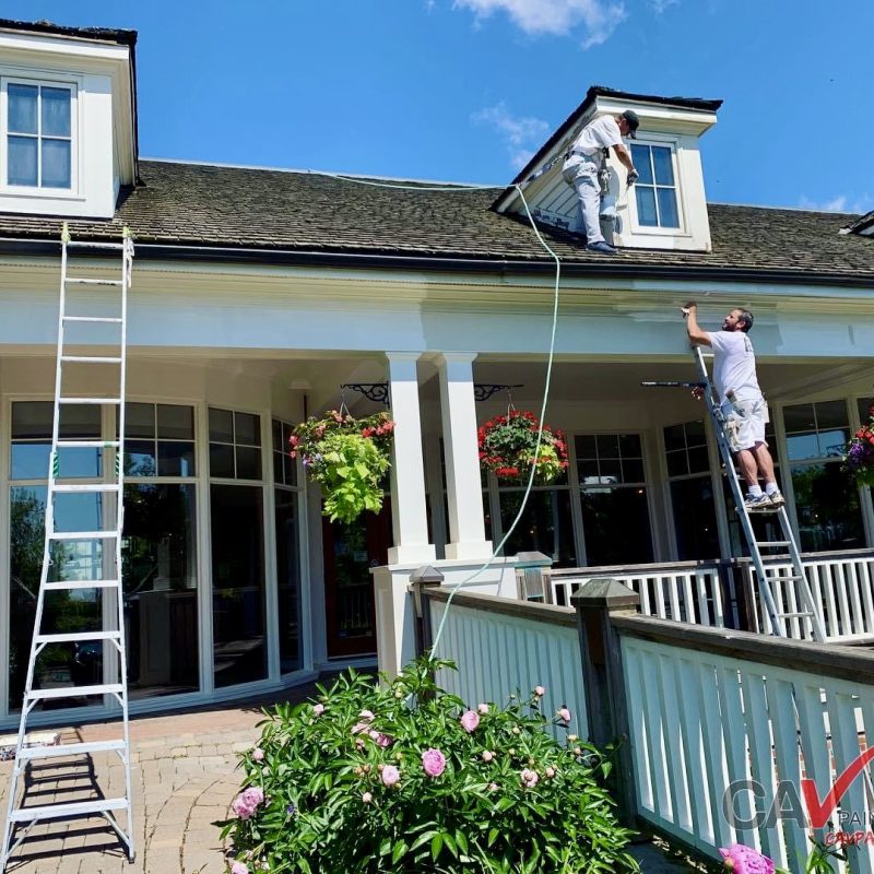 Team painting the exterior of a large house with ladders and safety gear.