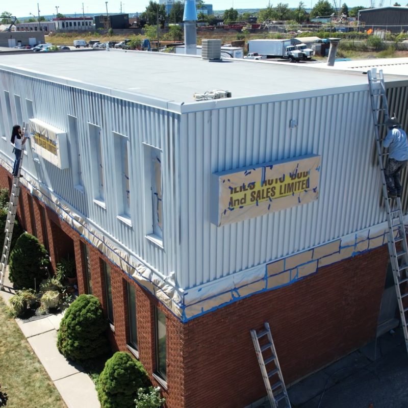 Painters using ladders to repaint the exterior siding of a commercial building.