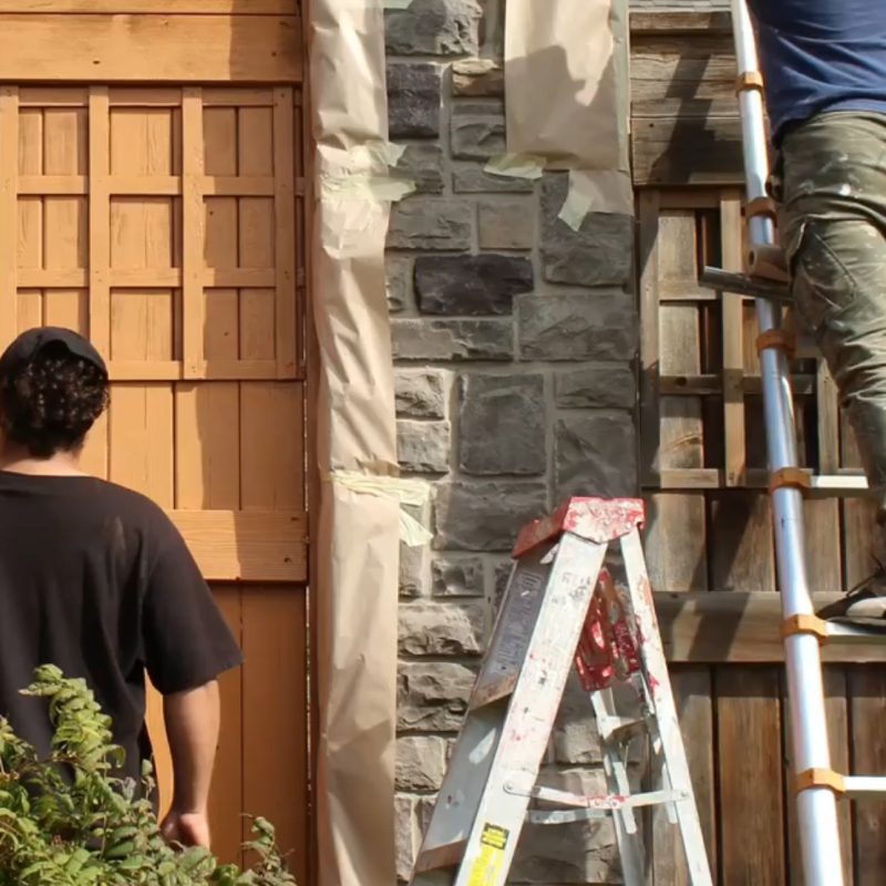 Workers masking stone columns with paper and tape before exterior painting.