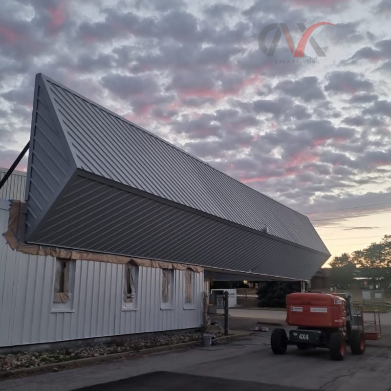 Industrial building exterior painted gray with lift equipment under a cloudy sky.