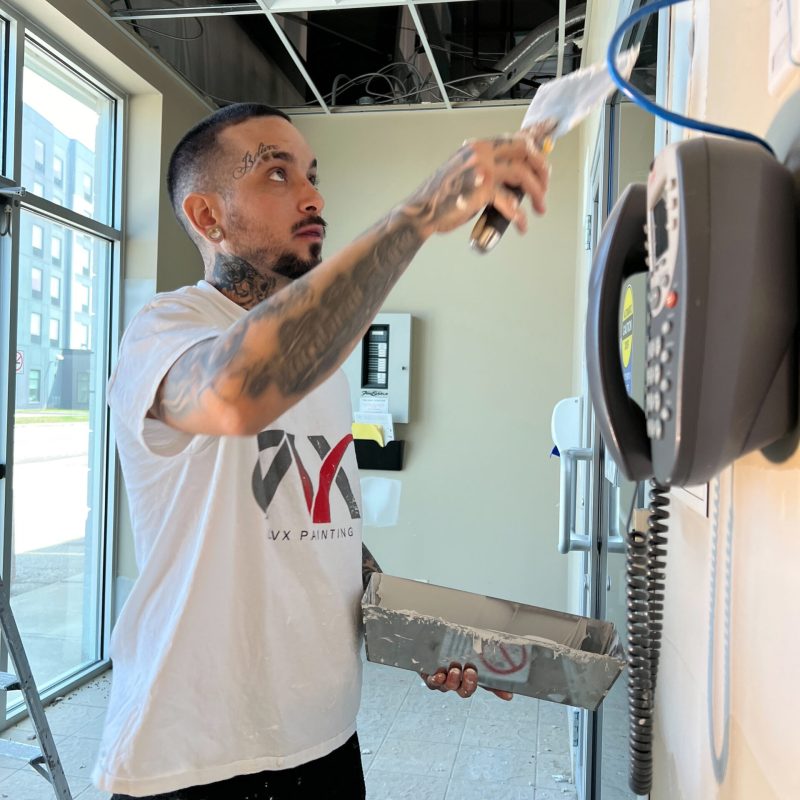 Painter applying wall paint near an office phone in a partially renovated space.
