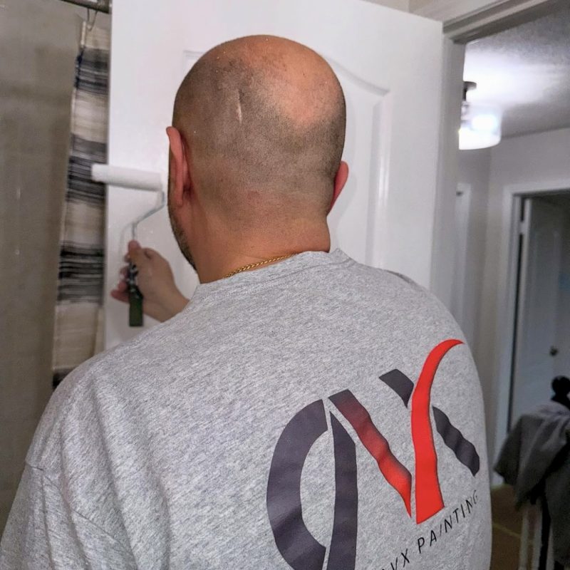 Painter using a small roller to coat a white door indoors.