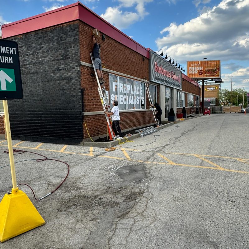 Painters on ladders repainting the facade of a commercial building.
